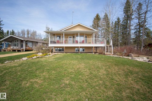 Elevated yellow-sided residence featuring a covered front porch with white railings - 77 Lakeshore Drive, Rural Leduc County, AB - Outdoor With Deck Patio Veranda