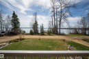Expansive property featuring a large body of water, mature evergreen trees, lush green lawn, and a white railing - 77 Lakeshore Drive, Rural Leduc County, AB  - Outdoor With View 