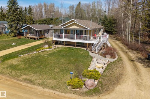 Elevated residence featuring a covered deck with white railings, a multi-level exterior staircase, and a gravel driveway - 77 Lakeshore Drive, Rural Leduc County, AB - Outdoor With Deck Patio Veranda