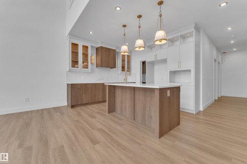 Modern kitchen featuring a central island with a white countertop, light wood-finish cabinetry, white upper cabinetry with open shelving, recessed lighting, and three pendant light fixtures - 13128 187 Avenue, Edmonton, AB - Indoor Photo Showing Kitchen