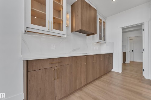 Modern kitchen featuring wood-finish lower cabinetry, white upper cabinetry with glass inserts, and a coordinating wood-finish range hood - 13128 187 Avenue, Edmonton, AB - Indoor Photo Showing Other Room