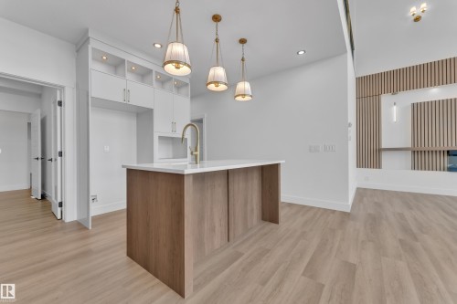 Kitchen island with a white countertop and wood-finish base, complemented by three brass-finish pendant lights - 13128 187 Avenue, Edmonton, AB - Indoor Photo Showing Kitchen