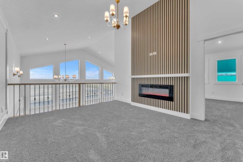 Carpeted upper-level space featuring a contemporary fireplace with a slatted wood-finish accent wall, vaulted ceilings, recessed lighting, and a chandelier - 13128 187 Avenue, Edmonton, AB - Indoor Photo Showing Other Room