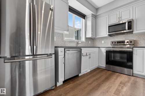 The kitchen features stainless steel appliances, light-colored cabinetry, and a patterned backsplash - 15 2072 Wonnacott Way, Edmonton, AB - Indoor Photo Showing Kitchen With Stainless Steel Kitchen With Upgraded Kitchen
