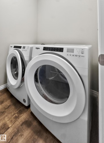 A dedicated laundry area featuring a front-loading washing machine and dryer, set against light-colored walls and wood-look flooring - 15 2072 Wonnacott Way, Edmonton, AB - Indoor Photo Showing Laundry Room