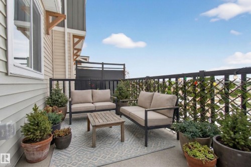 The property features an outdoor patio with a patterned area rug, black railings, and a lattice privacy screen - 15 2072 Wonnacott Way, Edmonton, AB - Outdoor With Deck Patio Veranda With Exterior