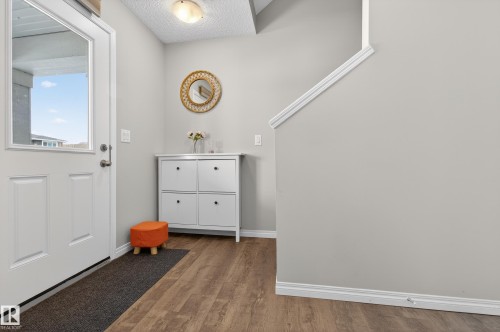 The entryway features a white front door with a window, wood-style flooring, and light gray walls - 15 2072 Wonnacott Way, Edmonton, AB - Indoor Photo Showing Other Room
