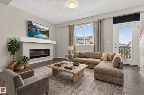 The property features a contemporary living area with a built-in fireplace, hardwood flooring, and a large window providing natural light - 15 2072 Wonnacott Way, Edmonton, AB - Indoor Photo Showing Living Room With Fireplace