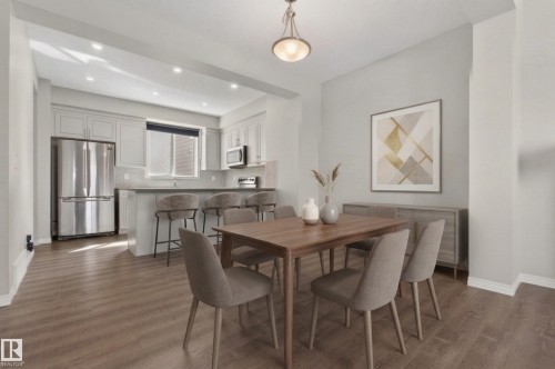 Dining area featuring hardwood style floors, a contemporary light fixture, and an open view to the kitchen - 15 2072 Wonnacott Way, Edmonton, AB - Indoor Photo Showing Dining Room