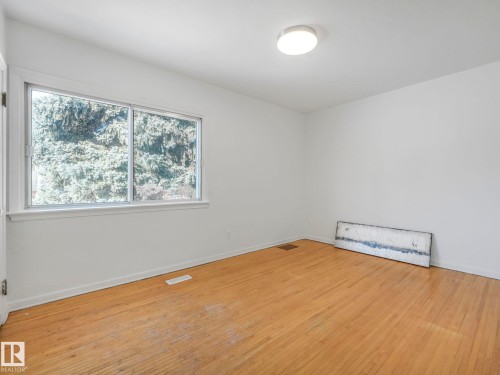 Room featuring light-colored hardwood floors, white walls, and a large window providing views of lush greenery - 10645 62 Avenue, Edmonton, AB - Indoor Photo Showing Other Room