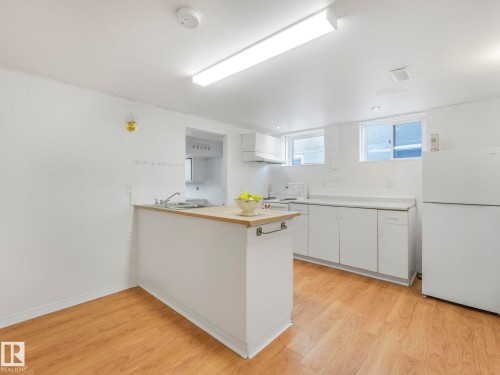 Kitchen featuring light-toned flooring, white cabinetry, a white refrigerator, and a breakfast bar with a wooden countertop - 10645 62 Avenue, Edmonton, AB - Indoor Photo Showing Kitchen