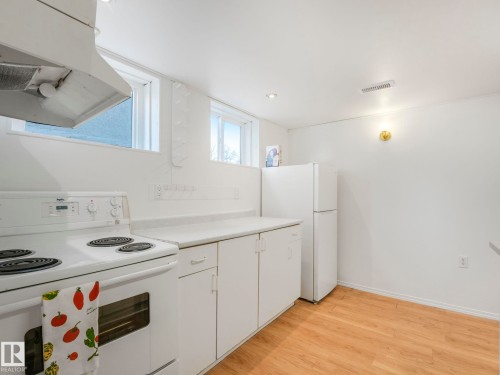 The kitchen features a white electric range, white cabinetry with a light-colored countertop, and a white refrigerator - 10645 62 Avenue, Edmonton, AB - Indoor Photo Showing Kitchen