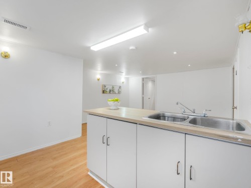 Kitchen area featuring a light-toned countertop with a double stainless steel sink, white cabinetry with dark handles, and light wood flooring - 10645 62 Avenue, Edmonton, AB - Indoor Photo Showing Kitchen With Double Sink