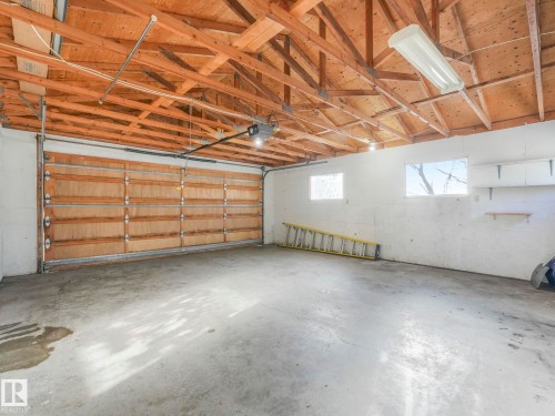Spacious garage featuring a concrete floor, exposed wood beams, and a wood panel garage door - 10645 62 Avenue, Edmonton, AB - Indoor Photo Showing Garage