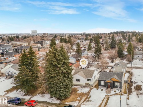 This aerial view showcases the property within a residential setting, featuring mature evergreen trees and surrounding neighborhood structures - 10645 62 Avenue, Edmonton, AB - Outdoor With View