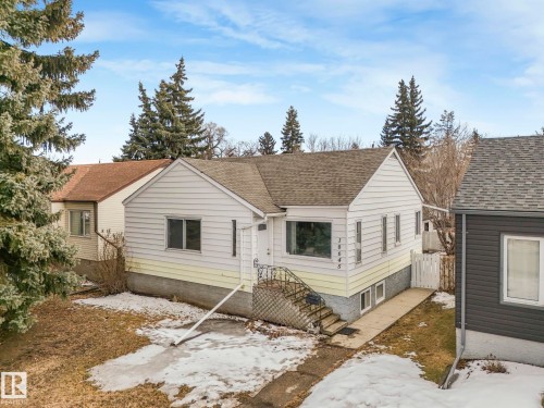 The property features white siding with a contrasting yellow lower section, a dark shingled roof, and a front porch with a dark railing and steps - 10645 62 Avenue, Edmonton, AB - Outdoor