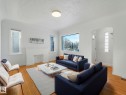 This living space features hardwood floors, white walls, and a large window overlooking a treed view - 10645 62 Avenue, Edmonton, AB  - Indoor Photo Showing Living Room 