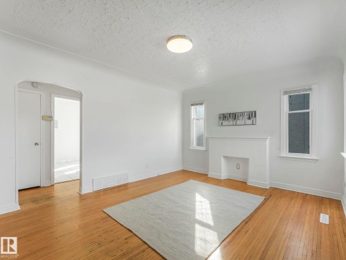 Living area featuring hardwood floors, a built-in decorative fireplace, and natural light from two windows - 10645 62 Avenue, Edmonton, AB - Indoor Photo Showing Other Room