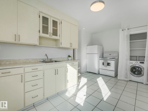 The kitchen features white cabinetry, a stainless steel sink, a refrigerator, and a stove - 10645 62 Avenue, Edmonton, AB - Indoor Photo Showing Laundry Room