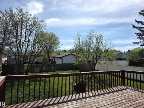 Wood deck with dark-stained railing, overlooking a fenced backyard with green lawn and mature trees - 4029 55 Avenue, Drayton Valley, AB - Outdoor
