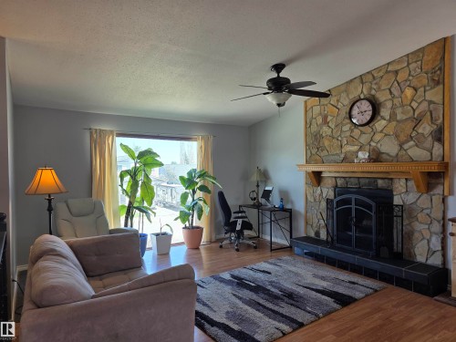Living area featuring a stone fireplace with a wood mantle, wood-finish flooring, and a ceiling fan with integrated lighting - 4029 55 Avenue, Drayton Valley, AB - Indoor Photo Showing Living Room With Fireplace