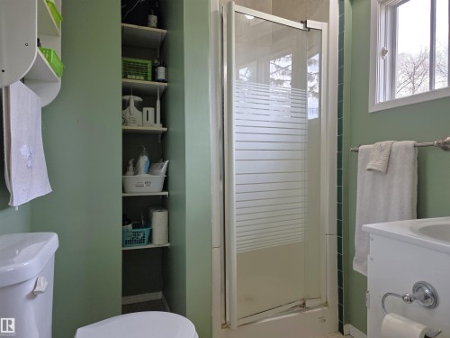 Full bathroom featuring a shower stall with a frosted glass door, a window with white trim, and a built-in shelving unit for storage - 4029 55 Avenue, Drayton Valley, AB - Indoor Photo Showing Bathroom