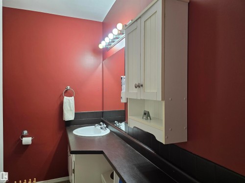 Bathroom vanity featuring a white oval sink, dark countertop, and a wall-mounted white storage cabinet - 4029 55 Avenue, Drayton Valley, AB - Indoor Photo Showing Bathroom