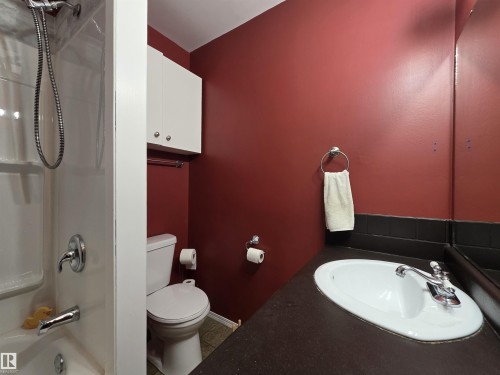 Bathroom featuring a white bathtub and shower combination with chrome fixtures, a white toilet, white wall-mounted cabinetry, a dark countertop with an integrated white sink, and a large wall-mounted mirror - 4029 55 Avenue, Drayton Valley, AB - Indoor Photo Showing Bathroom