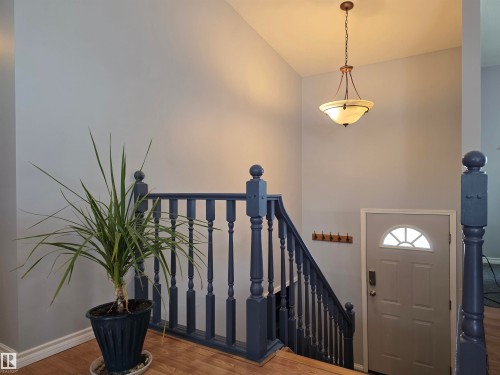 Entryway featuring a decorative pendant light fixture, wood-finish flooring, and a stairway with painted balusters - 4029 55 Avenue, Drayton Valley, AB - Indoor Photo Showing Other Room