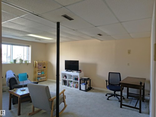 Carpeted living space featuring a drop ceiling with integrated lighting, a structural support column, and a window providing natural light - 4029 55 Avenue, Drayton Valley, AB - Indoor