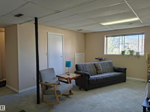 Carpeted interior space featuring a drop ceiling with integrated lighting, neutral wall tones, a white trim package, and a window with exterior visibility - 4029 55 Avenue, Drayton Valley, AB - Indoor