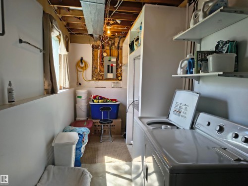 Dedicated utility area featuring a washer and dryer unit, ample wall shelving, exposed ceiling joists, and a visible electrical panel - 4029 55 Avenue, Drayton Valley, AB - Indoor Photo Showing Laundry Room