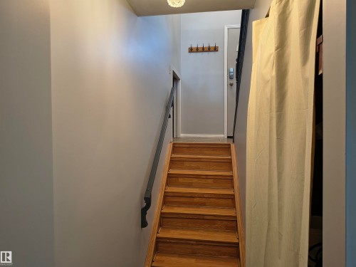 Hardwood stairs with a black metal handrail leading to a landing with a light gray painted wall and a wooden coat rack - 4029 55 Avenue, Drayton Valley, AB - Indoor Photo Showing Other Room