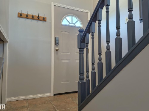 Entryway featuring a decorative front door with arched glass insert, tiled flooring, painted baluster staircase, and a wall-mounted coat rack - 4029 55 Avenue, Drayton Valley, AB - Indoor Photo Showing Other Room