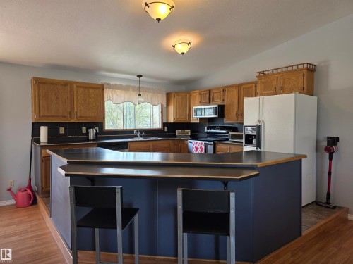 Kitchen with wood-finish flooring, oak cabinetry, and black countertops - 4029 55 Avenue, Drayton Valley, AB - Indoor Photo Showing Kitchen With Double Sink