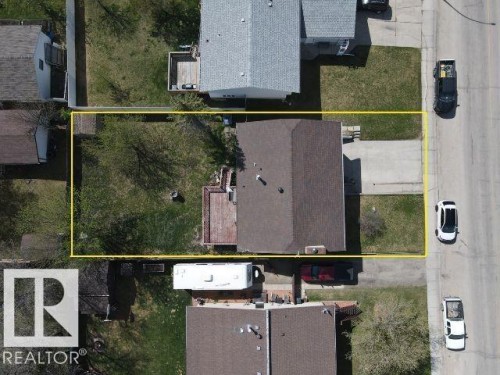 Residential property featuring a brown shingle roof, a concrete driveway, a rear wood deck, and a grass lawn with mature trees - 4029 55 Avenue, Drayton Valley, AB - Other