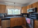 Kitchen featuring wood cabinetry, dark countertops, dark tile backsplash, a double basin sink, and stainless steel appliances including a dishwasher, range, and microwave - 4029 55 Avenue, Drayton Valley, AB  - Indoor Photo Showing Kitchen With Double Sink 