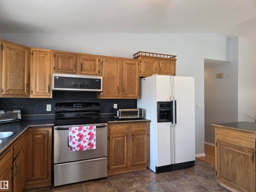 Kitchen featuring wood cabinetry, black countertops, a stainless steel range, and a built-in microwave - 4029 55 Avenue, Drayton Valley, AB - Indoor Photo Showing Kitchen