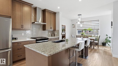 Contemporary kitchen featuring a large granite island, stainless steel appliances, sleek cabinetry, a subway tile backsplash, and wood-finish flooring - 17364 2 Street, Edmonton, AB - Indoor Photo Showing Kitchen With Double Sink With Upgraded Kitchen