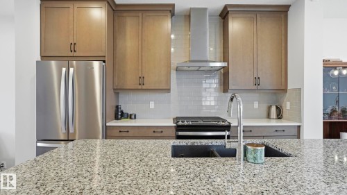 Spacious kitchen featuring an expansive speckled countertop, integrated sink with a gooseneck faucet, stainless steel appliances, and a subway tile backsplash - 17364 2 Street, Edmonton, AB - Indoor Photo Showing Kitchen With Double Sink With Upgraded Kitchen