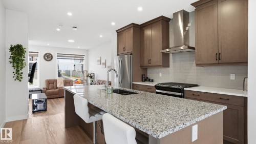 Open-concept kitchen featuring a spacious island with granite countertop, stainless steel appliances, modern cabinetry, subway tile backsplash, and wood-finish flooring - 17364 2 Street, Edmonton, AB - Indoor Photo Showing Kitchen With Upgraded Kitchen