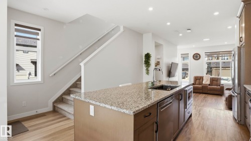 Open-concept living space with a central kitchen island featuring a granite-style countertop, a stainless steel sink with a high-arc faucet, and integrated appliances - 17364 2 Street, Edmonton, AB - Indoor Photo Showing Kitchen With Upgraded Kitchen