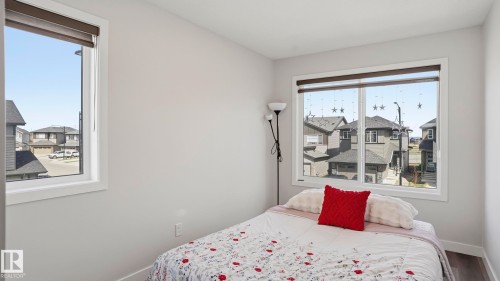 Light-filled interior featuring two windows with roller shades, neutral painted walls, and wood-finish flooring - 17364 2 Street, Edmonton, AB - Indoor Photo Showing Bedroom