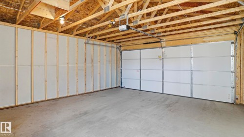 Spacious garage featuring exposed wooden rafters, a concrete floor, and a white paneled garage door with an automatic opener - 17364 2 Street, Edmonton, AB - Indoor Photo Showing Garage