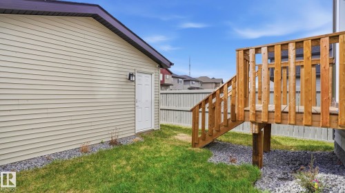 Outdoor deck with wooden railing and steps, alongside a beige siding structure with a side entrance door and exterior light fixture - 17364 2 Street, Edmonton, AB - Outdoor