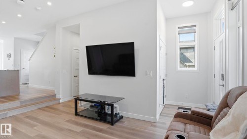 Open-concept living space featuring wood-finish flooring, recessed lighting, a modern built-in entertainment stand, a tall window, and a skylight - 17364 2 Street, Edmonton, AB - Indoor