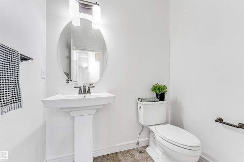 Pedestal sink with dark-toned faucet, complemented by an oval mirror and overhead vanity lighting - 2292 Casey Crescent, Edmonton, AB - Indoor Photo Showing Bathroom