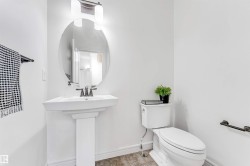 Pedestal sink with dark-toned faucet, complemented by an oval mirror and overhead vanity lighting - 