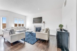 Spacious living area featuring wood-finish flooring, a white mantel fireplace with a glass-front insert, multiple windows, and recessed lighting - 