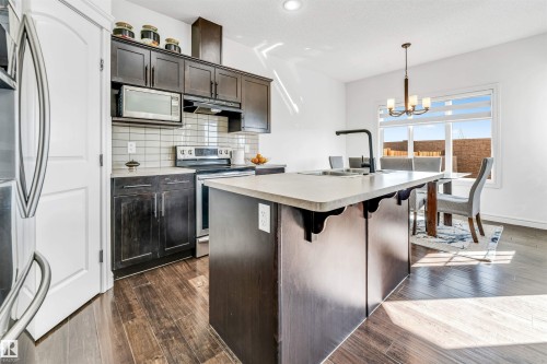 Kitchen featuring dark wood cabinetry, stainless steel appliances, and a light-colored island with an integrated sink - 2292 Casey Crescent, Edmonton, AB - Indoor Photo Showing Kitchen With Upgraded Kitchen